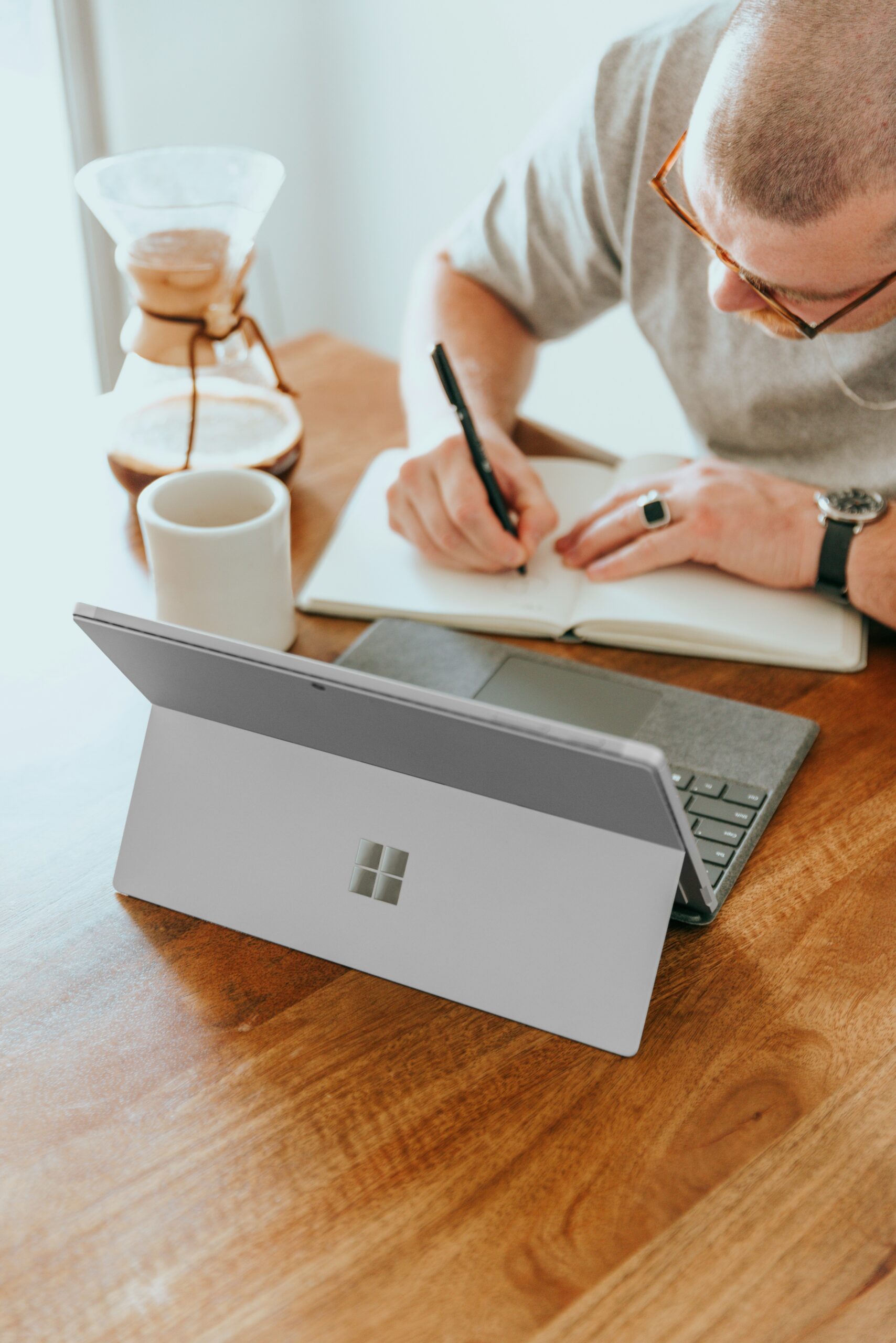 4-Ways-Small-Businesses-Can-Leverage-Microsoft-Copilot-for-SMBs-scaledjpg • Managed IT Services and Cybersecurity Provider in Singapore. a man sitting at a table writing on a notebook