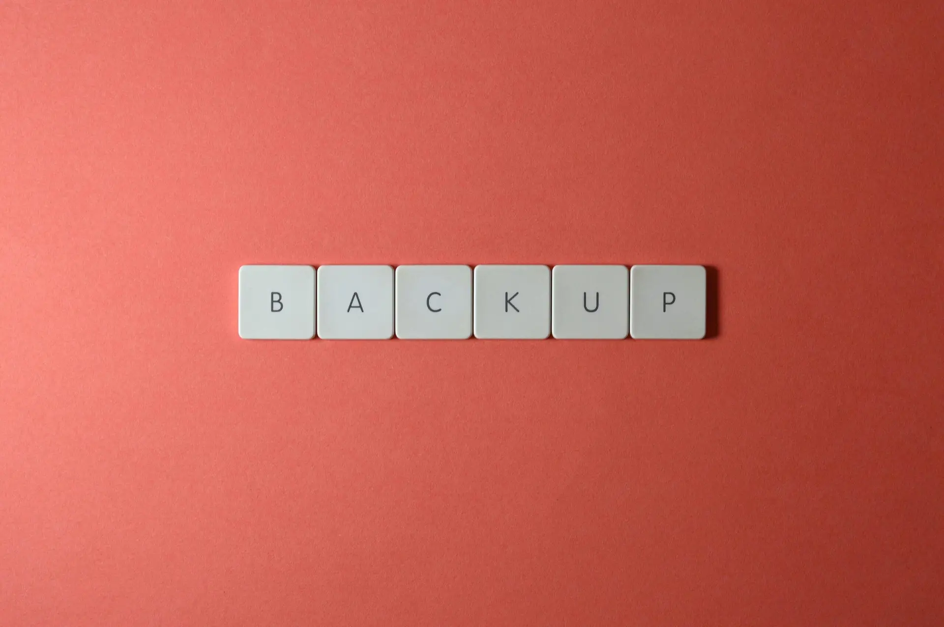 Free Close-up of keyboard keys spelling 'BACKUP' placed on a coral-colored surface. Stock Photo