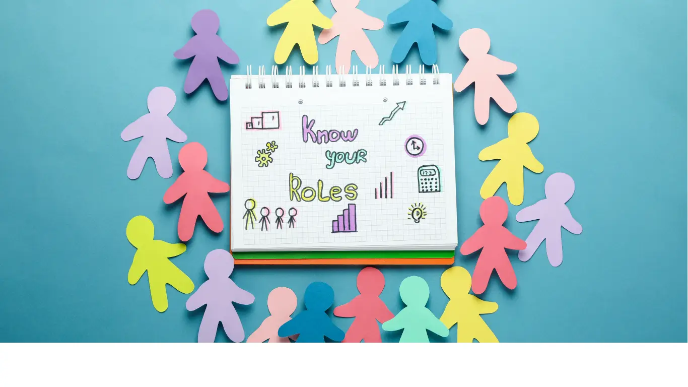Notebook page titled 'Know your Roles' with doodles, surrounded by colorful paper cut-out people on a blue background (teamwork concept).