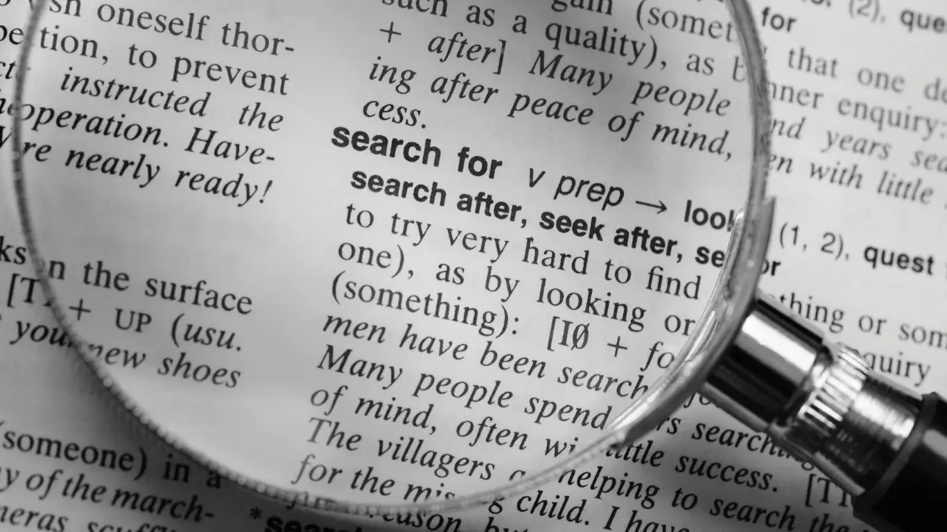 Magnifying glass held over a page of text, highlighting the word 'search' to symbolize searching or close reading.
