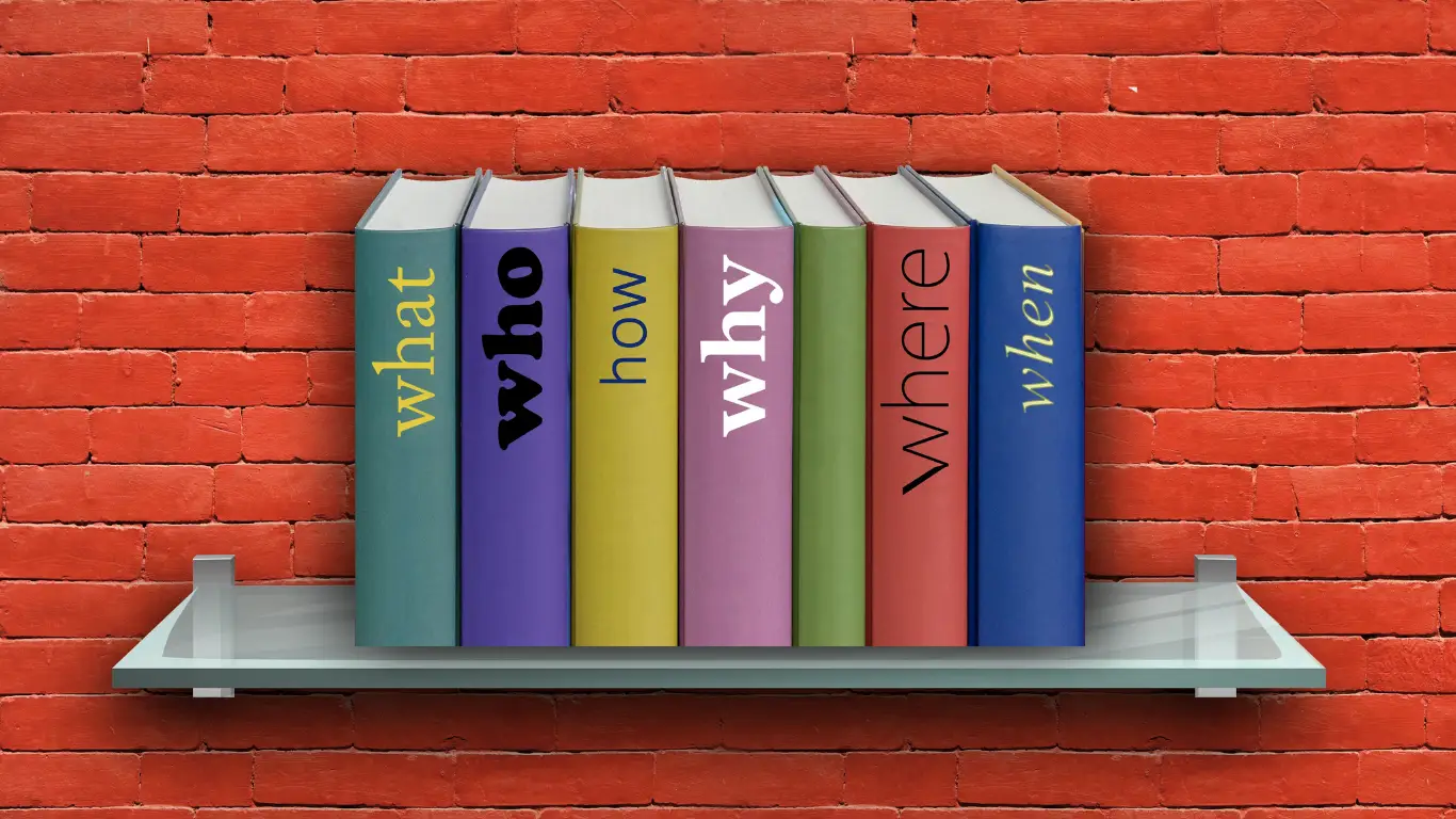 Row of colorful hardcover books on a glass shelf against a red brick wall; vertical spines spell What, Who, How, Why, Where (from left to right).