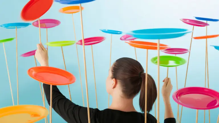 Person seen from behind adjusting colorful plate sculptures on tall sticks in a bright blue space